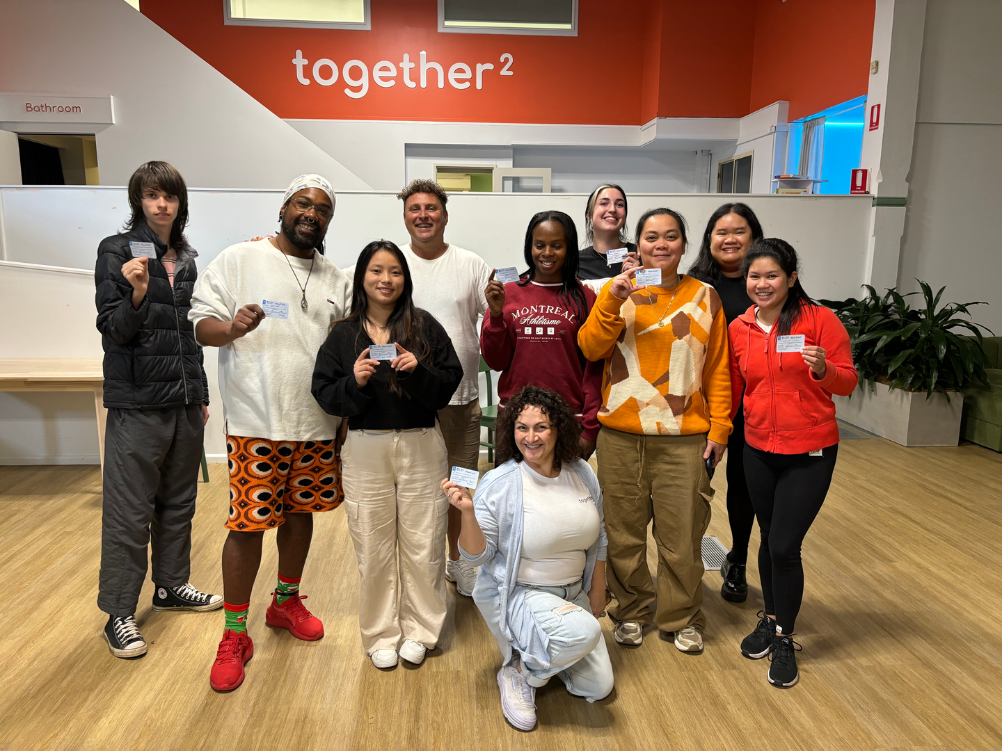 The together² team in our Rozelle hub, holding their First Aid certifications, in front of the together² brand wall